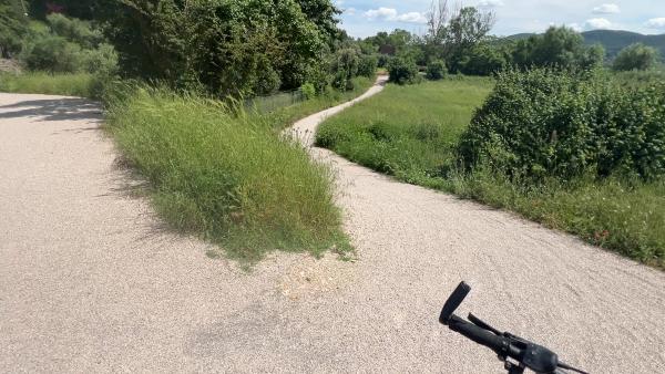 Scharfe und steile Kurve auf dem Radweg. Schotterweg zwischen Bäumen und Feldern.